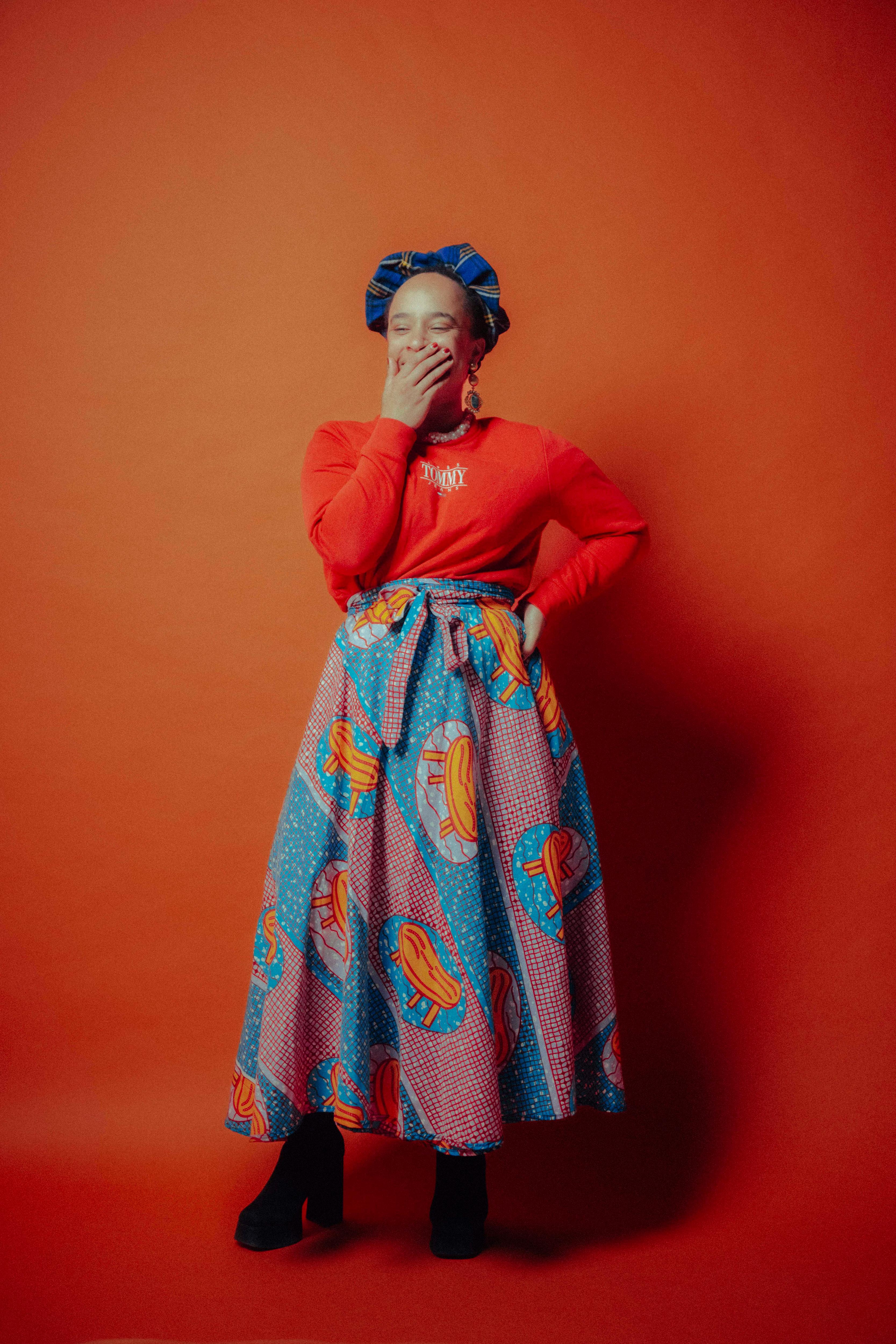 Nkechi Anele does a little giggle against an orange background 