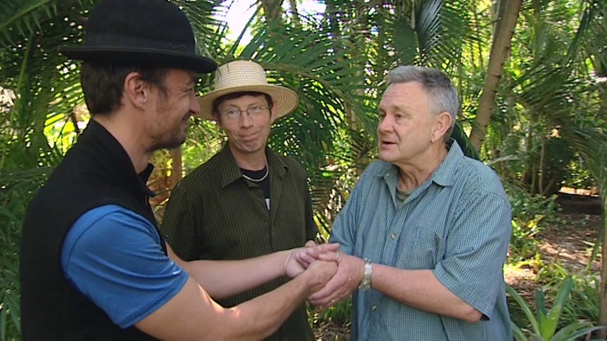 Man holding another man's hands to thank him with other man looking on