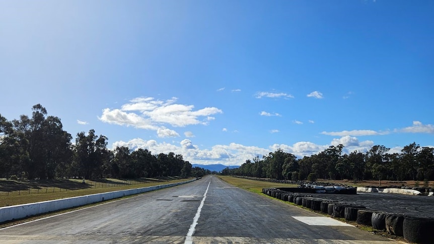 An empty race track extending into the distance with blue sky and clouds above.  