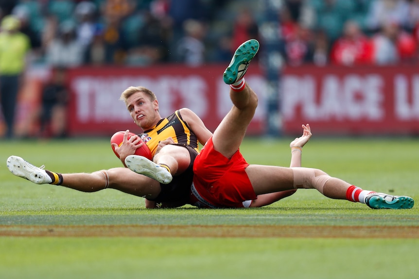 A Hawthorn AFL player o n the ground after being tackled by a Sydney Swans opponent.