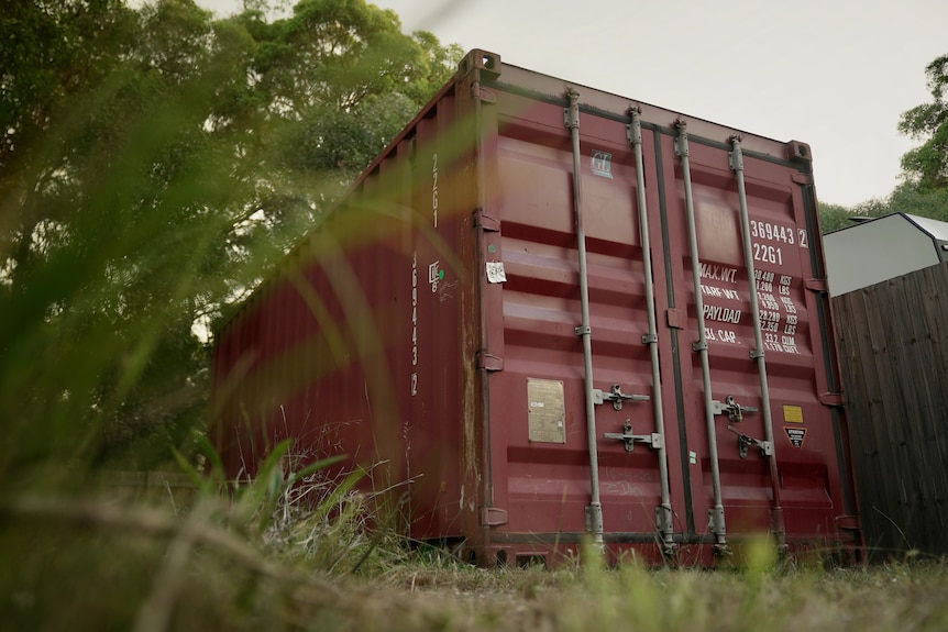 A maroon shipping container in grass.