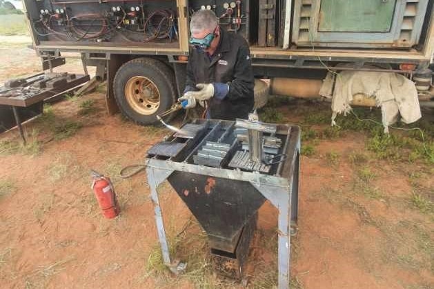 A man with grey hair works at a welding table.