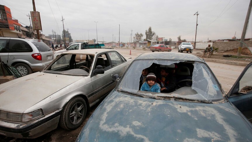 Children peer through a broken windshield of a car in Mosul.