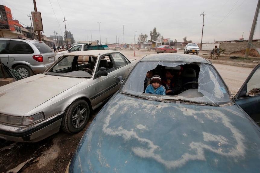 Children peer through a broken windshield of a car in Mosul.