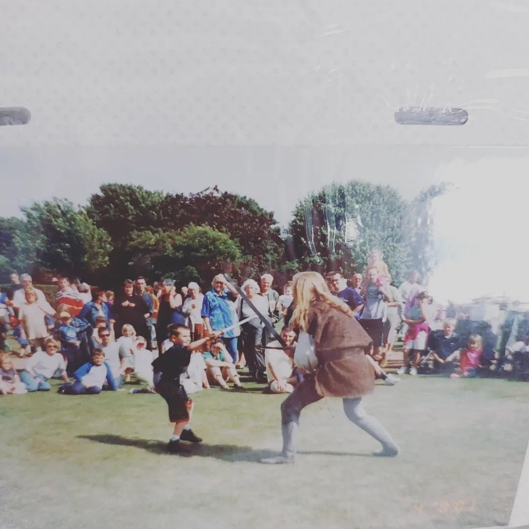 Young boy sword fighting with an older man on a grass field in Scotland.