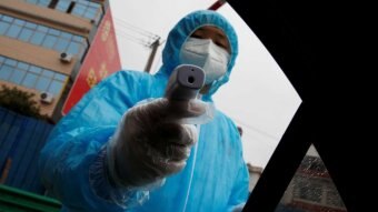 A medical worker holds a thermometer to check a passenger's temperature at a checkpoint.