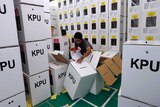 Stacks of Indonesian ballot boxes tower over a man who is struggling to grip one as it falls to the floor.
