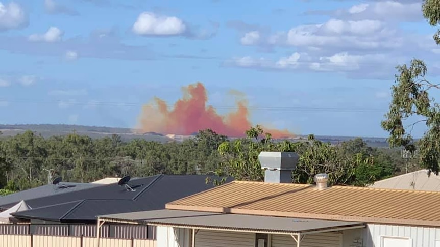 An orange and red plume of chemical, dust and smoke can be seen from houses.