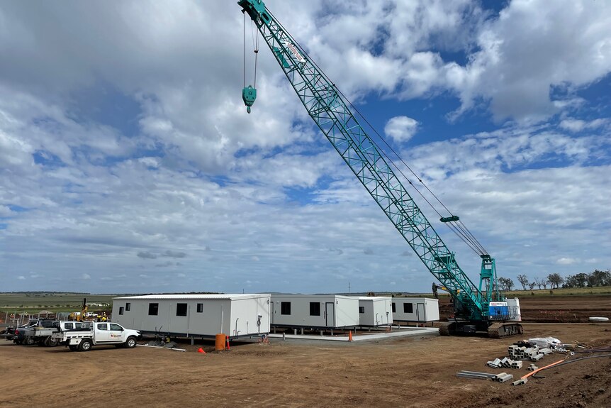 A row of demountable buildings and a crane on dirt.