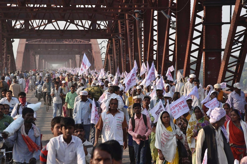Hindu pilgrims hold religious flags and walk on a crowded bridge after a stampede.
