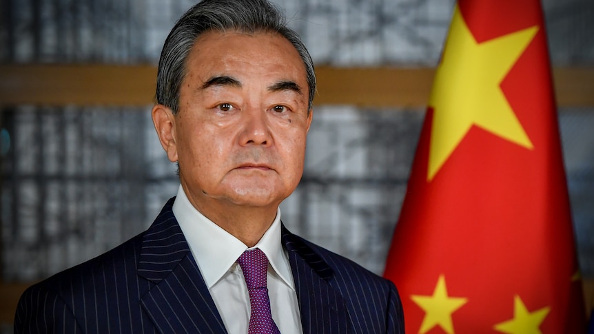 Chinese Foreign Minister Wang Yi stands in front of a Chinese flag