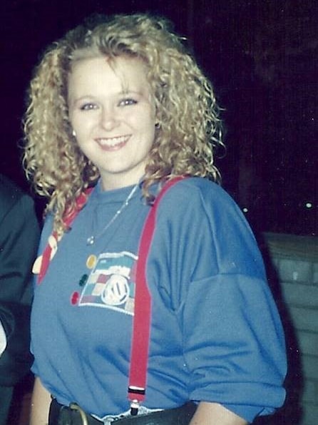 A young Suzi Dent wearing a baggy blue top and red braces holding up her jeans