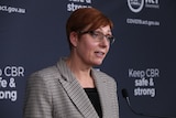 A woman with short red hair stands at a lectern