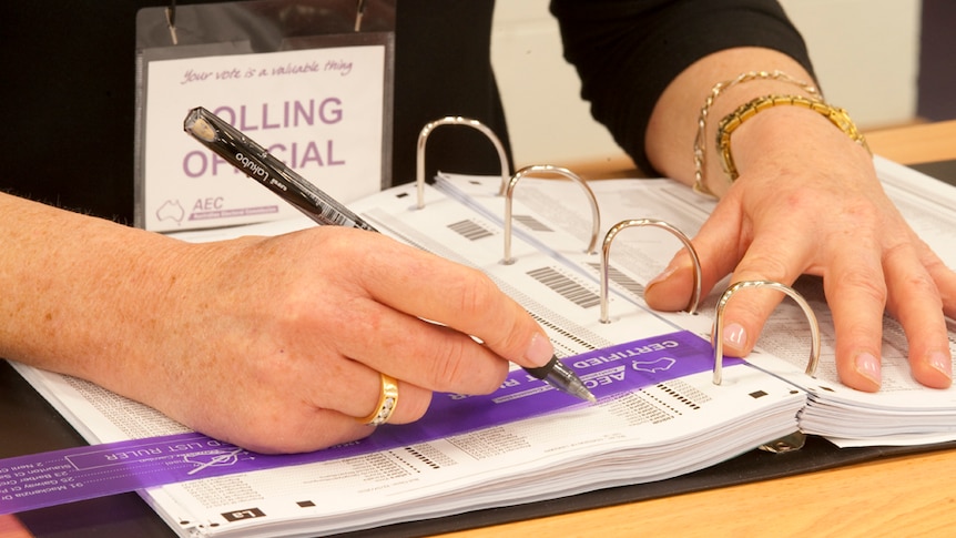 A polling official uses a pen to mark a name off the voting list.