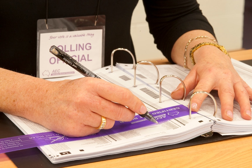A polling official uses a pen to mark a name off the voting list.