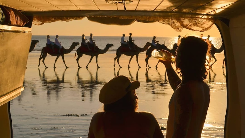 Two people sit in the back of a van, watching the camels on Cable Beach at sunset.