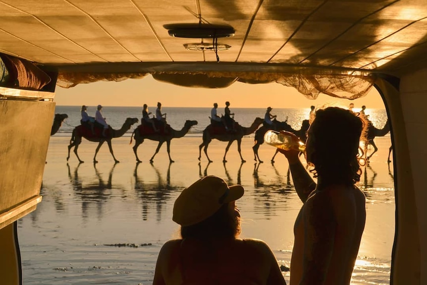 Two people sit in the back of a van, watching the camels on Cable Beach at sunset.