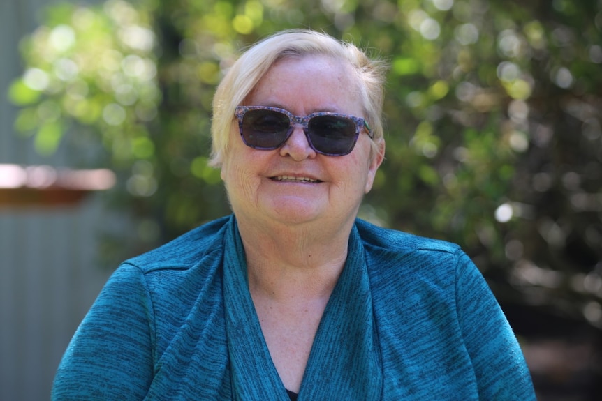 An older woman with short blonde hair wearing sunglasses and a blue blouse