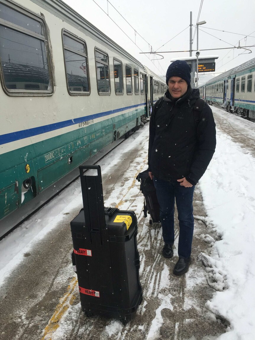Cannane standing in snow on train station in Italy with camera gear in pelican case.