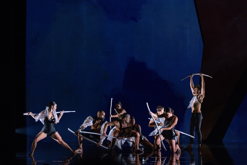 A stage of dancers, powerfully moving holding sticks on stage 
