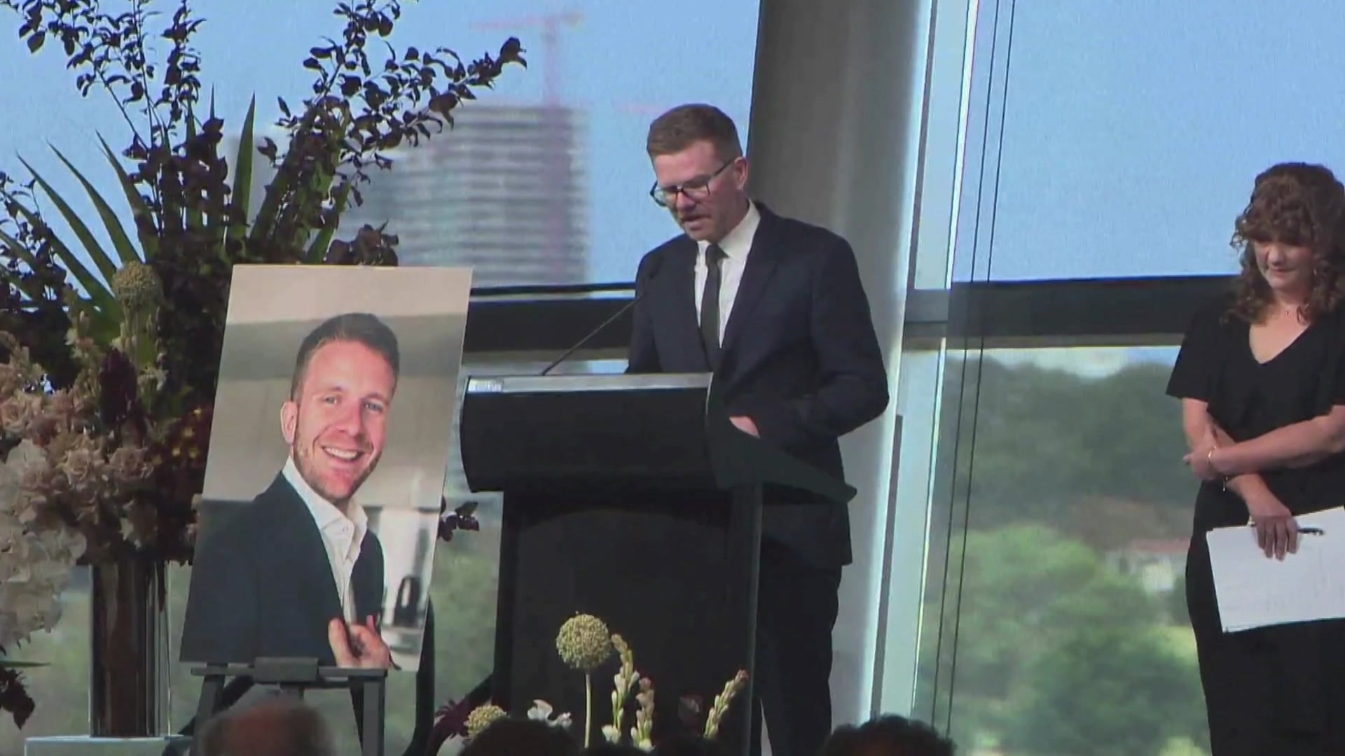 Un hombre de traje habla ante un atril frente al cual se muestra una fotografía de gran tamaño.