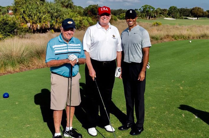 Donald Trump stands in between Jack Nicklaus and Tiger Woods on a golf course. Mr Trump is wearing his red USA cap.