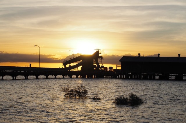 Derby wharf at high tide is silhouetted by a setting sun, with water in the foreground.