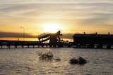 Derby wharf at high tide is silhouetted by a setting sun, with water in the foreground.