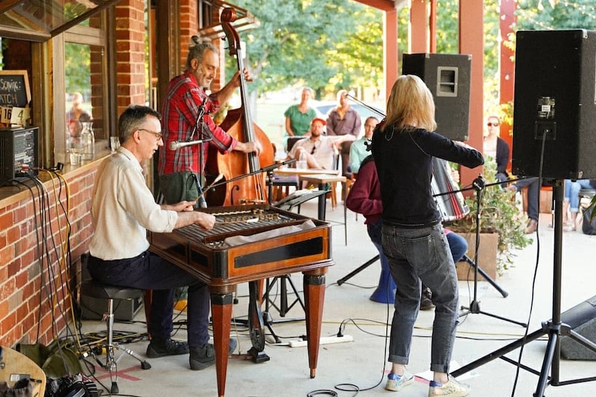A band plays under an awning to a group of seated people outside the cafe.