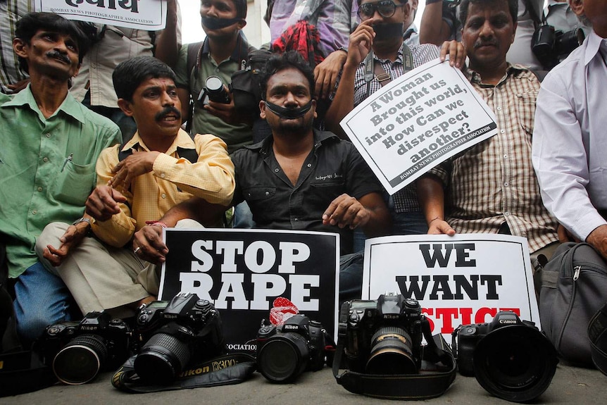 A group of Indian journalists sit on the ground with their cameras in front of them in a protest against sexual violence.