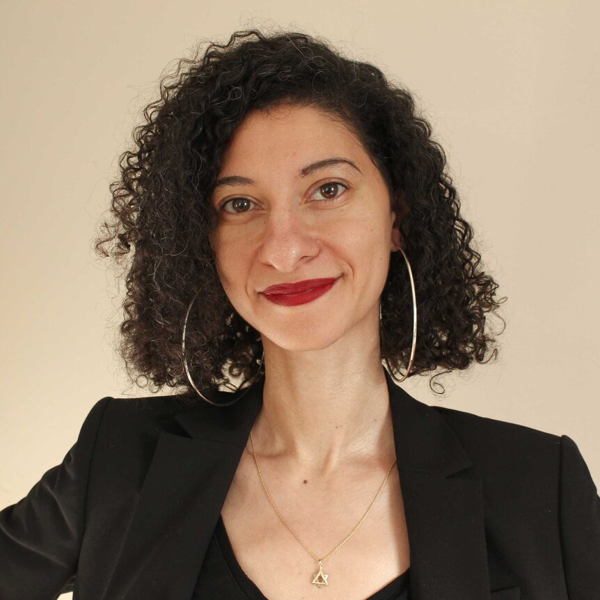 Woman with curly dark hair, large hoop earrings, black jacket and necklace with Star of David charm on it