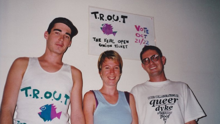 An old photo of people smiling with a sign that reads TROUT