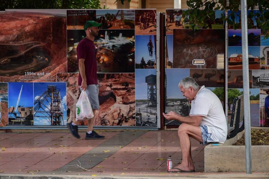 A young walking and and an older man sitting on the streets of Cobar.