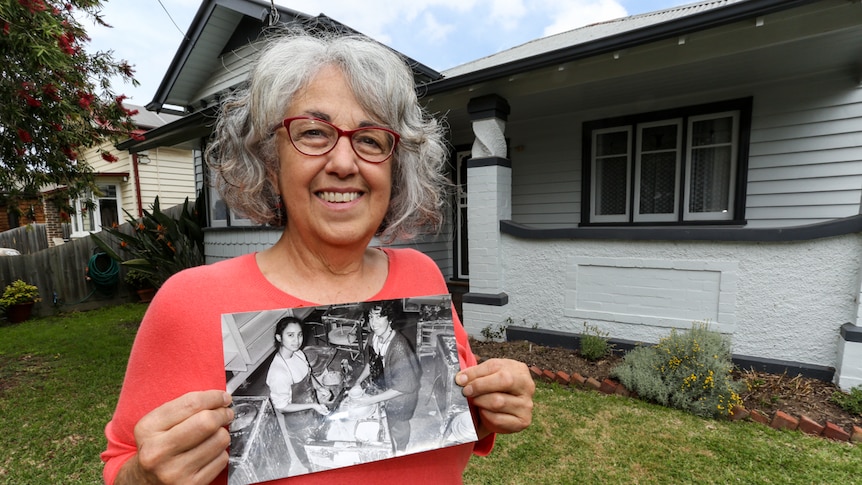 Carmella Savale standing in front of her house holding a photograph of her teaching pottery.