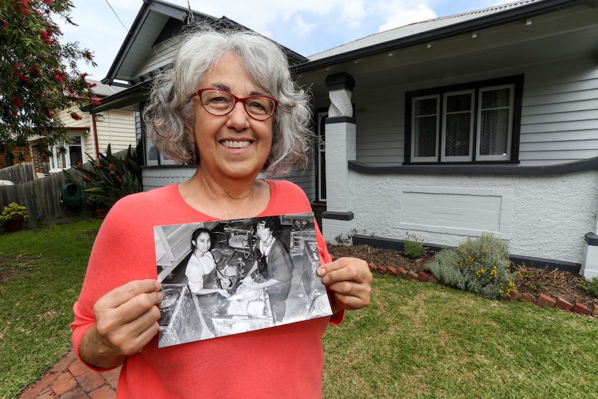 Carmella Savale standing in front of her house holding a photograph of her teaching pottery.
