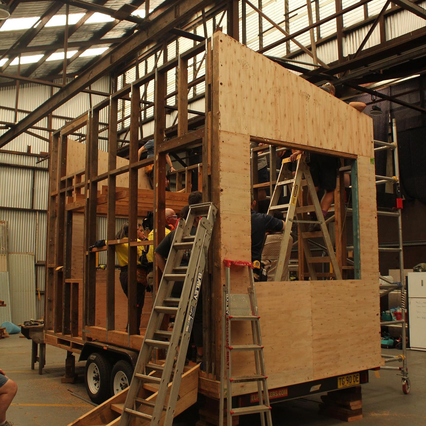 A half-finished tiny home with people on a ladder inside and holes for windows.