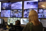 A woman watches an array of screens displaying CCTV feeds in a call centre