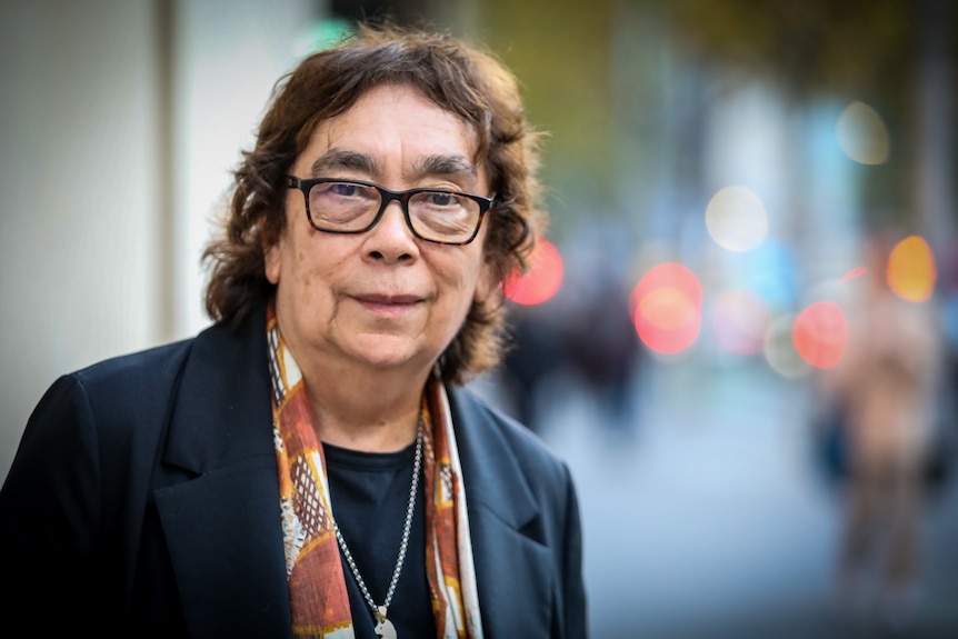 An older Indigenous woman with shaggy brown hair and glasses wearing a navy blazer