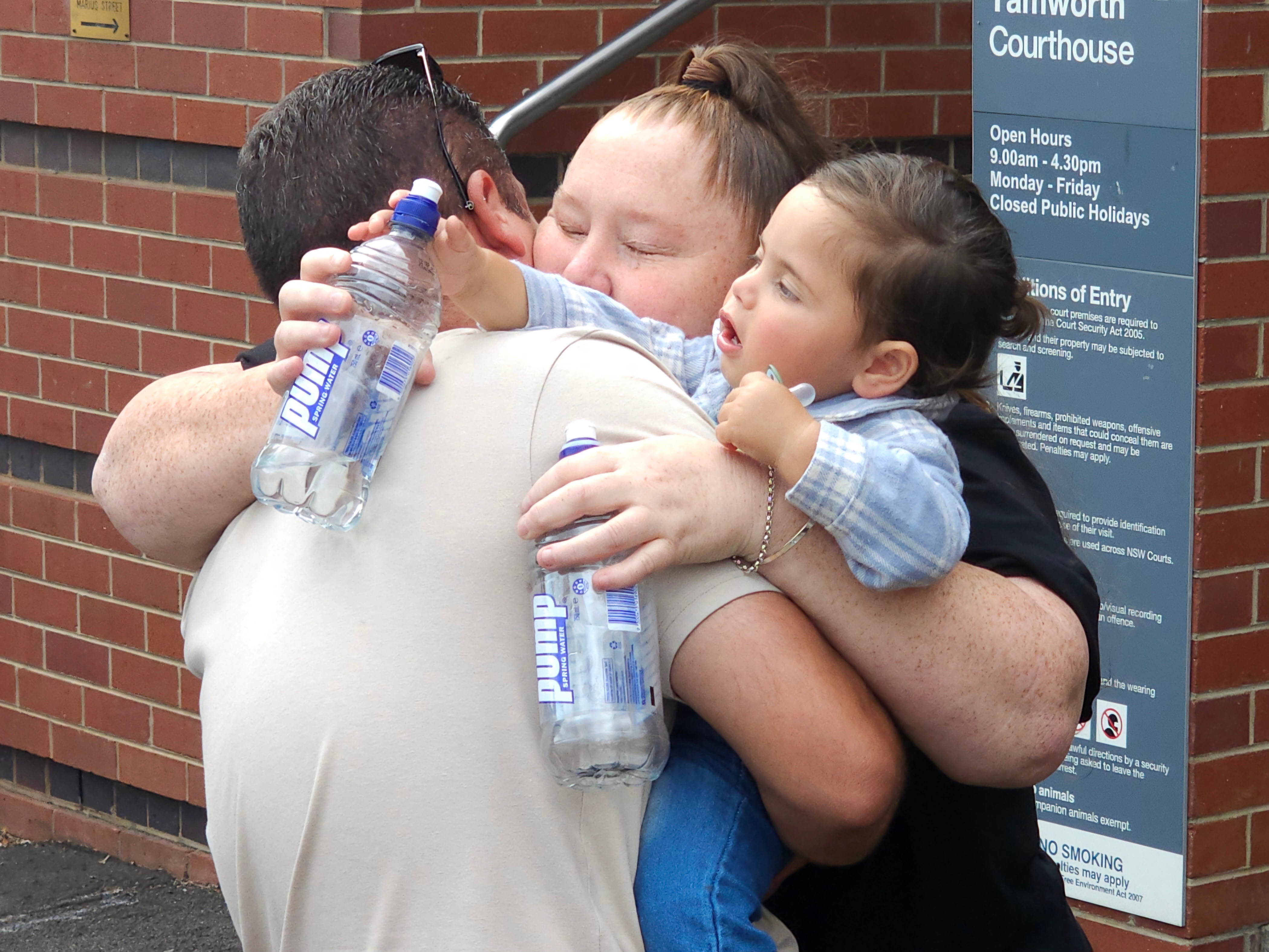 A man and woman hug, in their arms a young child plays with water bottles