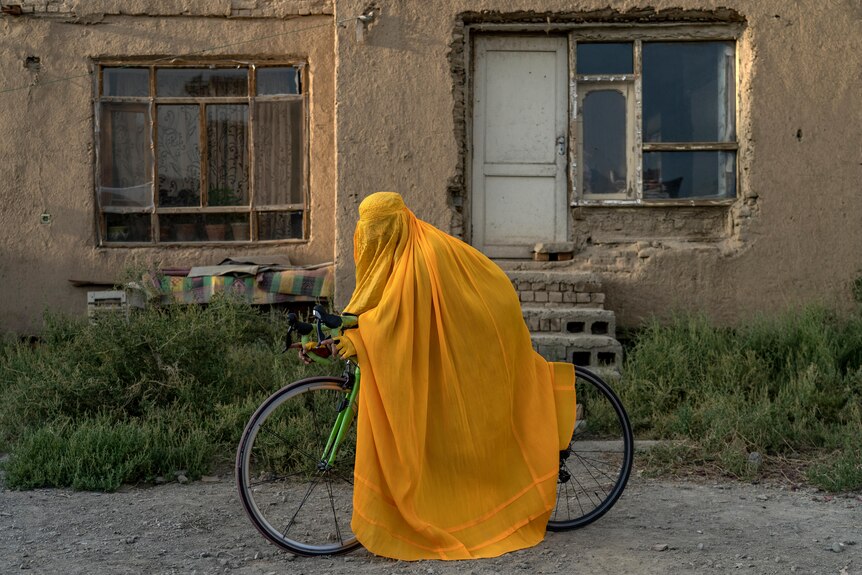 在喀布尔，一名穿着罩袍的阿富汗妇女骑着自行车摆姿势拍照。