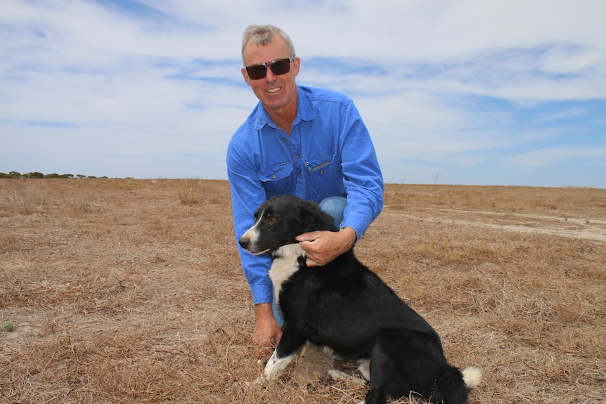 Man and dog pose in paddock of dried pasture