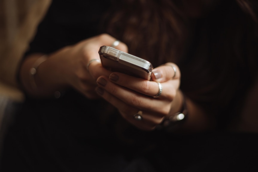 Female hands holding a mobile phone with a dark background.