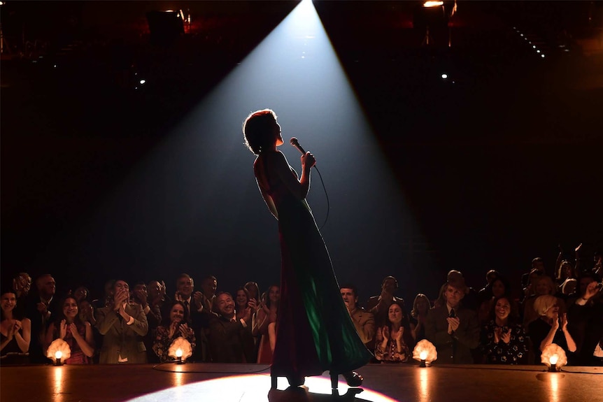 The silhouette of a woman with a microphone singing on stage.