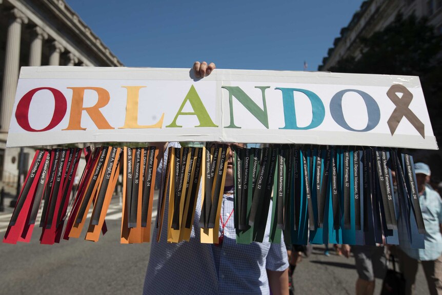 A man carries a rainbow coloured sign which reads "Orlando" and includes the names of all the Pulse victims
