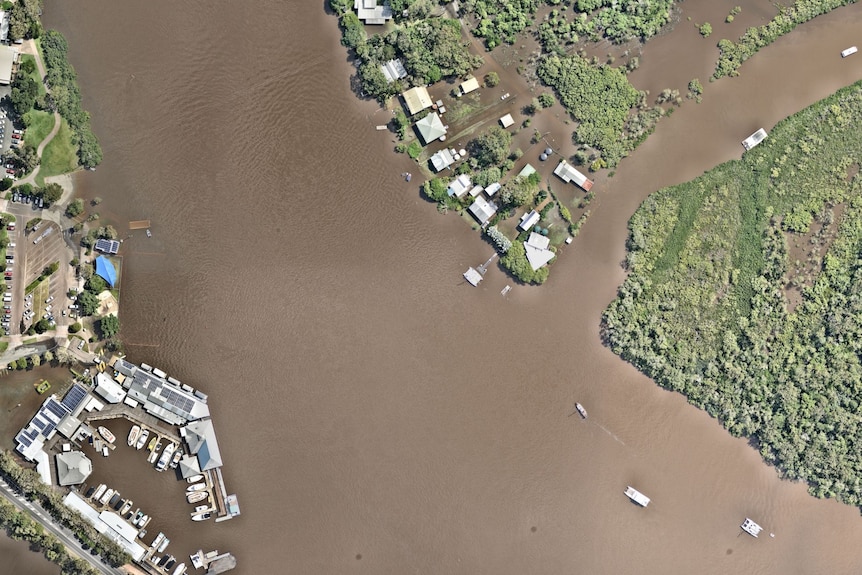The flooded Noosa River, and buildings along its banks including the Tweantin Noosa River, are seen from above.