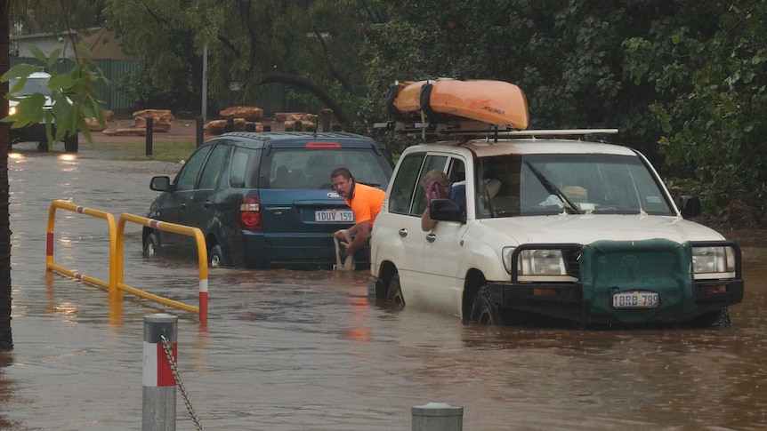 A man in hi-vis attaches a tow rope to a four wheel drive to get a car out of flood waters.