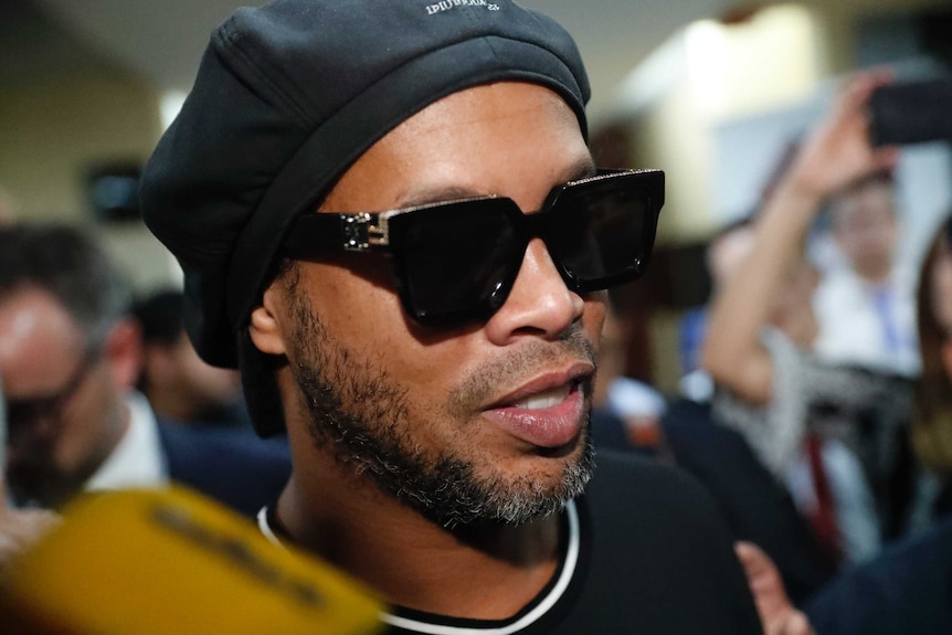 Former Brazilian soccer star Ronaldinho wears sunglasses as people try to take photos of him walking through the crowd.