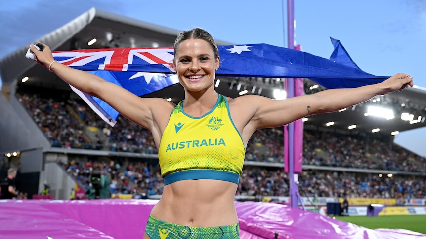 A woman smiles as she holds an Australian flag.