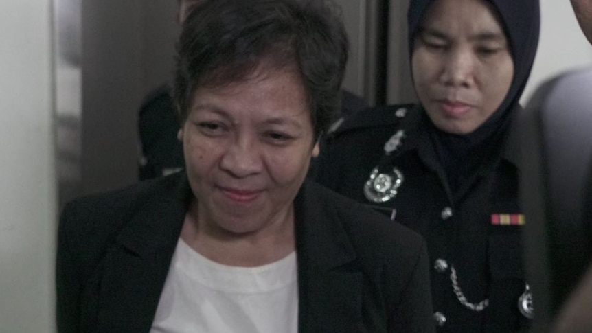 Maria Exposto smiles slightly as she is escorted into a Malaysian court by authorities.