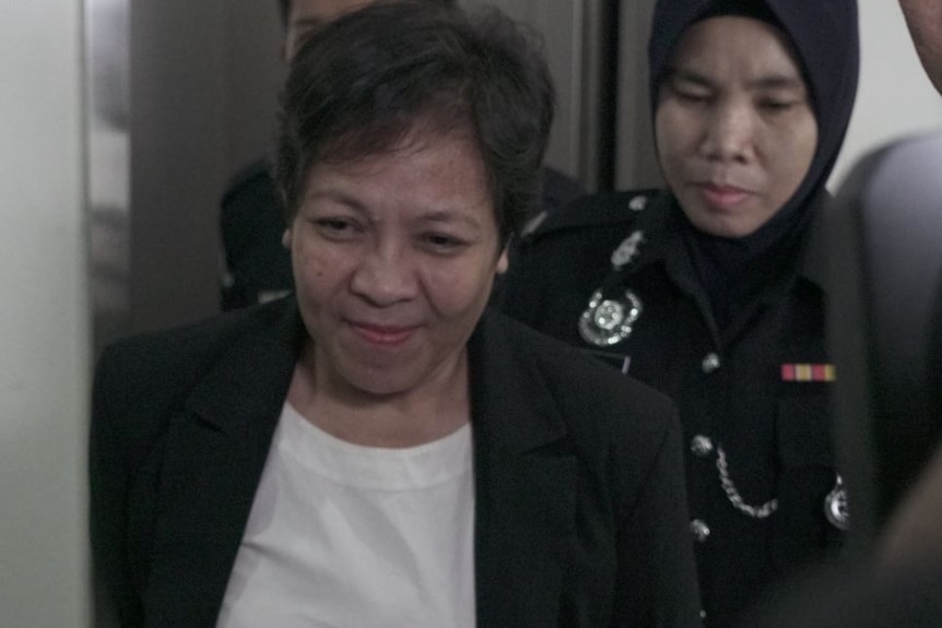 Maria Exposto smiles slightly as she is escorted into a Malaysian court by authorities.